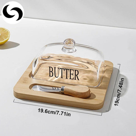 Light brown bamboo butter dish with a clear lid, butter label, and matching spreader tool on a 19.6cm by 19cm wooden base.
