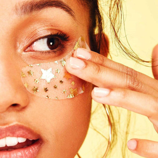 Woman applying a translucent hydrogel under-eye patch decorated with shimmering gold star patterns.