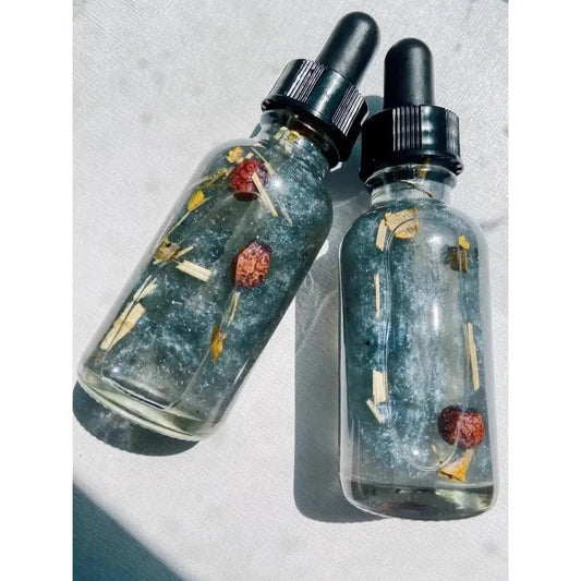 Two glass dropper bottles filled with shimmering blue oil, dried botanicals, and rosehips on a white background.
