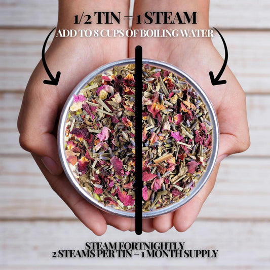Hands holding a tin of organic yoni steam herbs featuring dried rose petals, lavender, and botanical leaves.