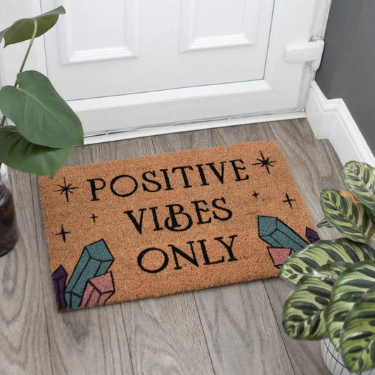 Natural coir doormat with Positive Vibes Only text, star accents, and colorful crystal illustrations on a wooden floor.