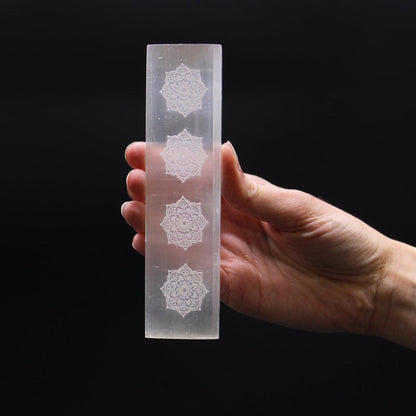Hand holding a translucent white selenite charging plate engraved with four intricate mandala designs.