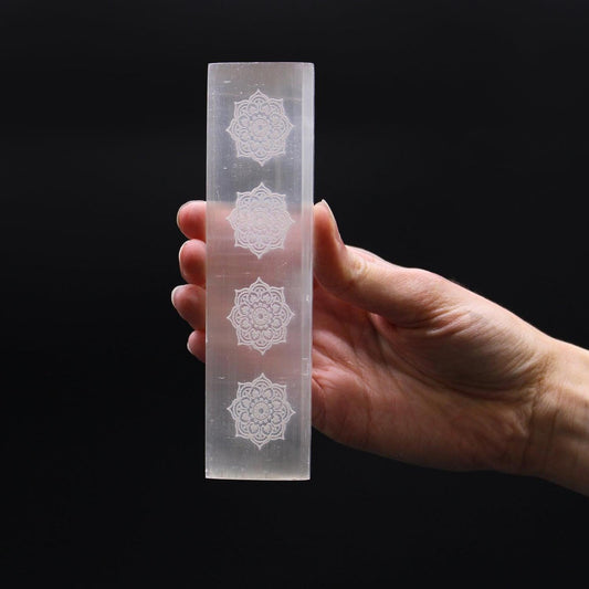 Hand holding a translucent white selenite charging plate engraved with four intricate mandala designs.