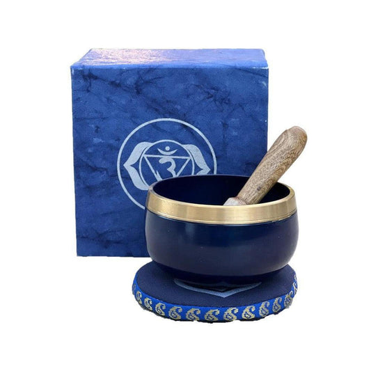 Midnight blue singing bowl with brass rim, wooden striker, and matching Third Eye chakra gift box on a blue cushion.