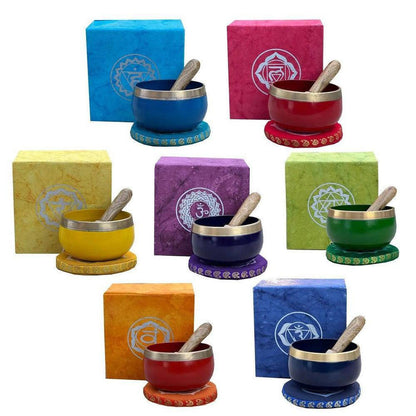 Set of seven colorful chakra singing bowls with wooden strikers, matching gift boxes, and embroidered cushions.