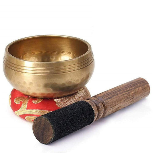 Handcrafted copper Tibetan singing bowl with a wooden striker on a decorative red and gold silk cushion.